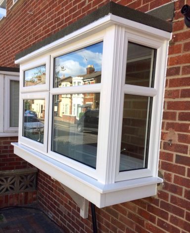 White bay window with multiple glass panels, set against a brick wall background.