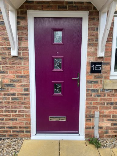 A purple front door with three glass panes, set against a brick wall. House number 15 displayed.