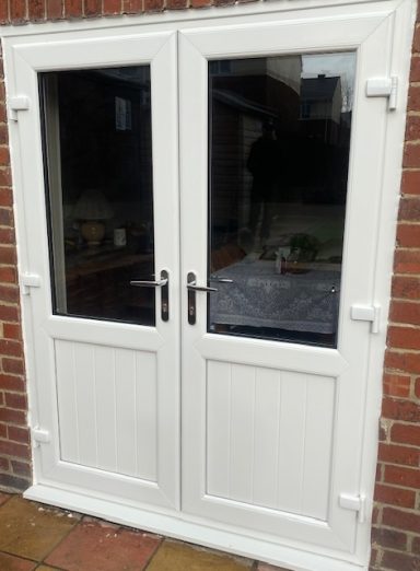 French, sliding and bi-fold door range White double doors with glass panels, framed in a brick wall.
